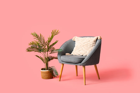 Modern gray armchair with pillow and flowerpot on pink backgroundの写真素材