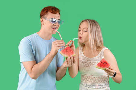 Young beautiful man with woman holding slices of fresh watermelon and straws on green backgroundの写真素材