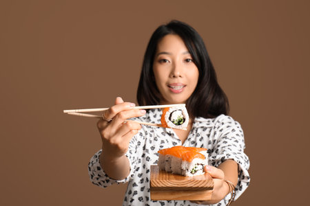 Pretty young Asian woman with set of tasty Philadelphia rolls on brown backgroundの写真素材