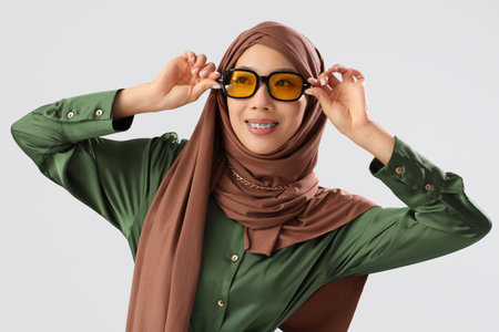 Beautiful young Asian woman in hijab and sunglasses on gray backgroundの写真素材