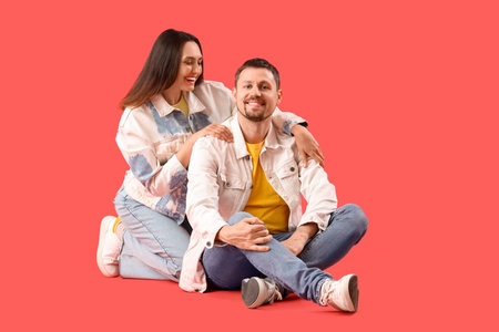 Happy young couple sitting on red backgroundの写真素材