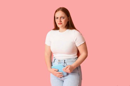 Young woman with hot water bottle having menstrual cramps on pink backgroundの写真素材