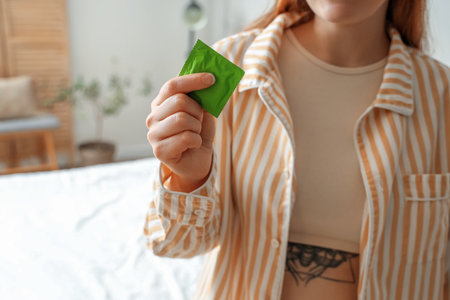 Young woman with condom in bedroom, closeupの写真素材
