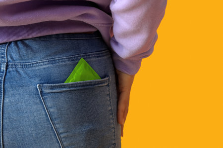 Young woman with condom in pocket on orange background, back viewの写真素材