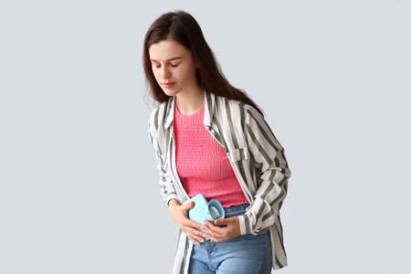 Young woman having menstrual cramps on light background