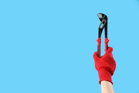 Female hand in red glove holding waterpump pliers on blue backgroundの写真素材