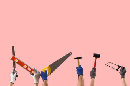 Female and male hands holding different construction tools on pink backgroundの写真素材