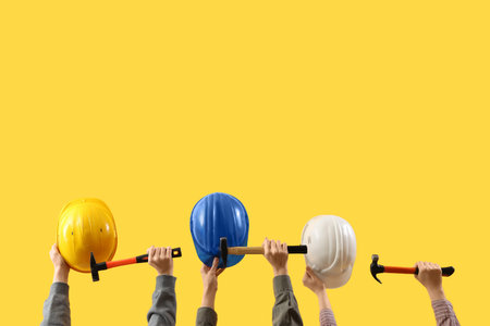 Female hands holding safety hardhats and hammers on yellow background