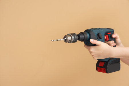 Female hands holding rotary hammer with drill on beige backgroundの写真素材