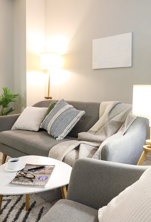Interior of living room with cozy gray sofa, armchair and glowing lamp