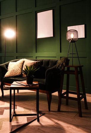 Interior of dark living room with green sofa, coffee table and glowing lampsの写真素材