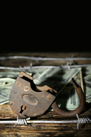 Lock with barbed wire and dollar banknotes on dark wooden table, closeup. Sanctions conceptの写真素材