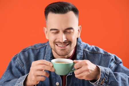Handsome man with cup of tea on orange background, closeupの写真素材