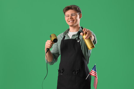 Male hairdresser with USA flag, blow drier and sprayer bottle on green backgroundの写真素材