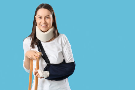 Injured young woman after accident with crutch on blue backgroundの写真素材