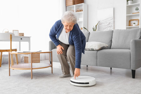 Senior woman with robot vacuum cleaner at homeの写真素材