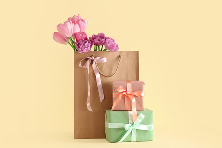Paper bag with beautiful tulips and gift boxes on yellow background. Mother's Day celebrationの写真素材