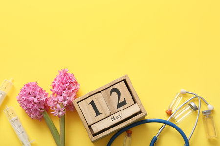 Calendar with flowers, stethoscope and ampules for International Nurses Day on yellow backgroundの写真素材
