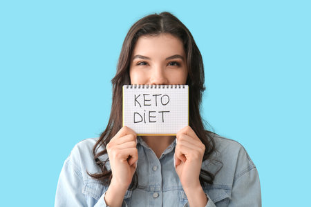 Beautiful young woman holding notebook with text KETO DIET on blue backgroundの写真素材