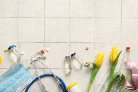 Stethoscope with mask, ampules and yellow tulips for International Nurses Day on white tile backgroundの写真素材
