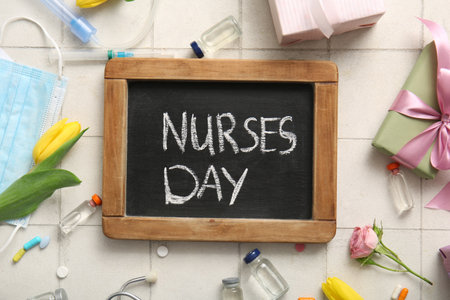 Chalkboard with text NURSES DAY, gift boxes and medical items on white tile backgroundの写真素材