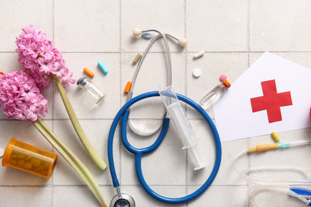Stethoscope with paper medical hat, pills and flowers for International Nurses Day on white tile backgroundの写真素材