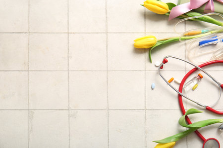 Stethoscope with catheter, pills and yellow tulips for International Nurses Day on white tile backgroundの写真素材