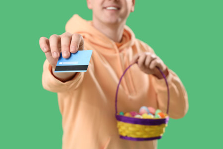 Young man with credit card and basket on green background, closeup. Easter Saleの写真素材