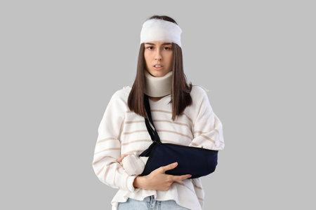 Injured young woman after accident with broken arm on light backgroundの写真素材
