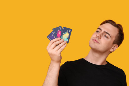 Young man with credit cards on yellow backgroundの写真素材