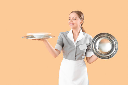 Young waitress with empty plate, tray and cloche on beige backgroundの写真素材