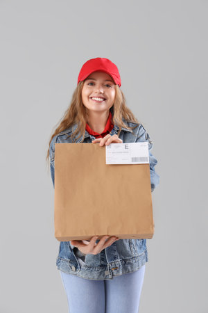 Beautiful young woman holding paper bag on gray background. Food deliveryの写真素材