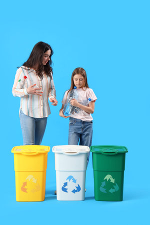 Little girl with her mother throwing plastic bottles in recycle bin on blue background