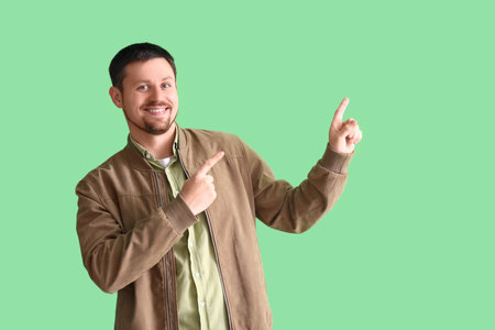 Handsome man pointing at something on green backgroundの写真素材
