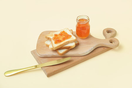 Wooden boards of tasty toasts, apricot jam and knife on pale yellow backgroundの写真素材