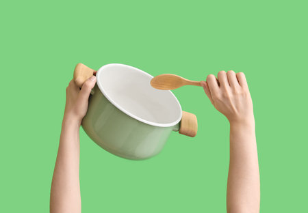 Woman with cooking pot and spoon on green background