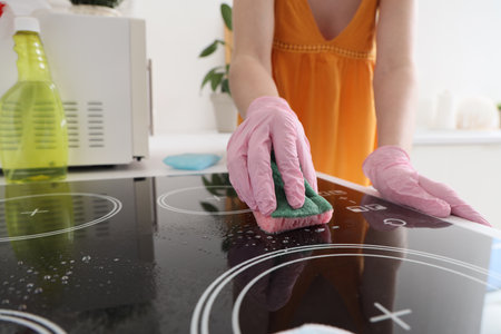 Woman cleaning electric stove with sponge in kitchen, closeupの写真素材