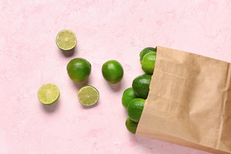 Paper bag with fresh limes on pink background