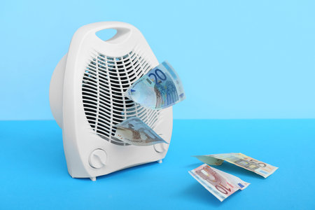 Electric fan heater with euro banknotes on blue tableの写真素材