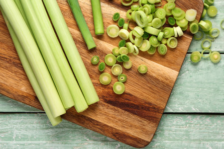 Board with slices of fresh leek on green wooden background