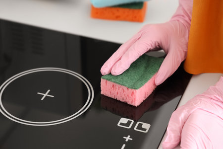 Woman cleaning electric stove with sponge in kitchen, closeupの写真素材