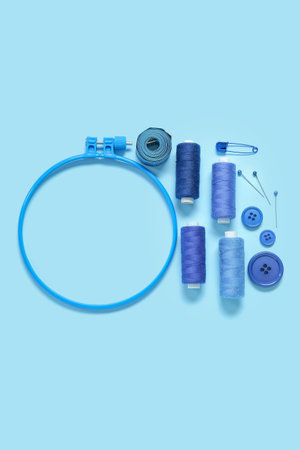 Embroidery hoop with thread spools, buttons and measuring tape on blue background