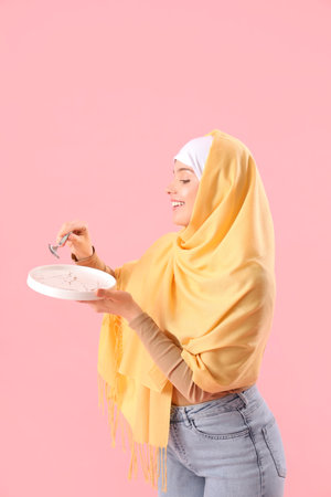 Beautiful Arabian woman with empty plate and spoon on pink backgroundの写真素材