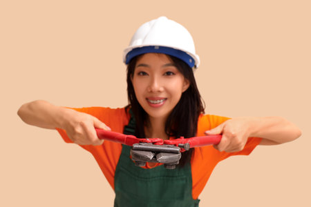 Asian woman in jumpsuit and hardhat with bolt cutter on beige backgroundの写真素材