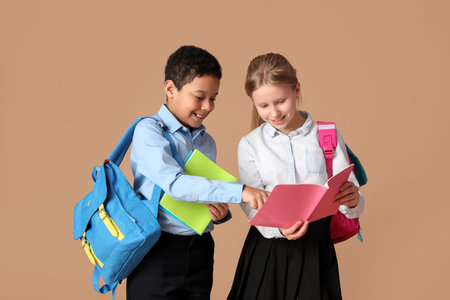 Cute children in school uniform with backpacks and copybooks on beige background