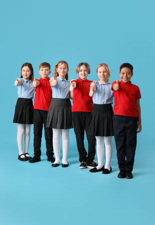 Group of cute children in school uniform showing thumb-up on blue backgroundの写真素材