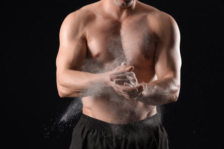 Muscular male bodybuilder clapping hands with chalk powder on black backgroundの写真素材