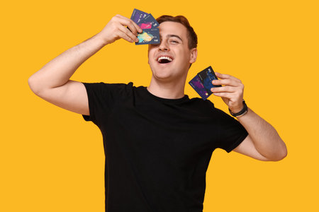 Young man with credit cards on yellow background