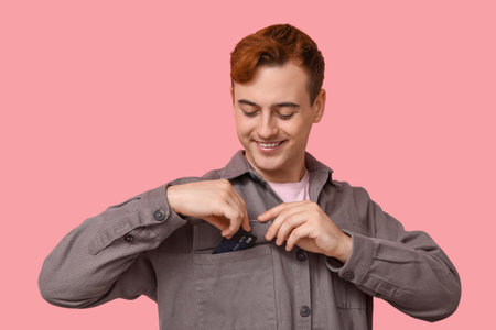 Young man putting credit card into pocket on pink backgroundの写真素材