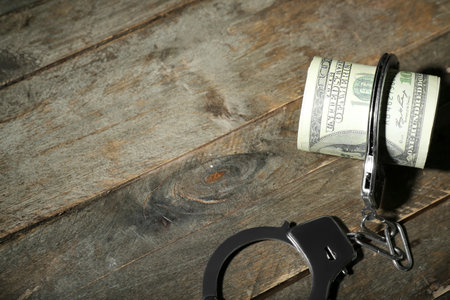 Handcuffs with dollar banknotes on dark wooden background. Sanctions conceptの写真素材